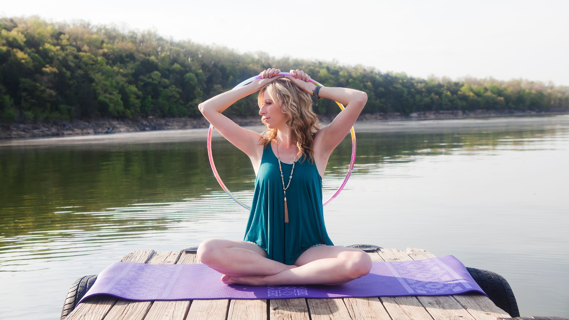 Michele McCoy sitting with hoop above head by lake, hoop dance instructor