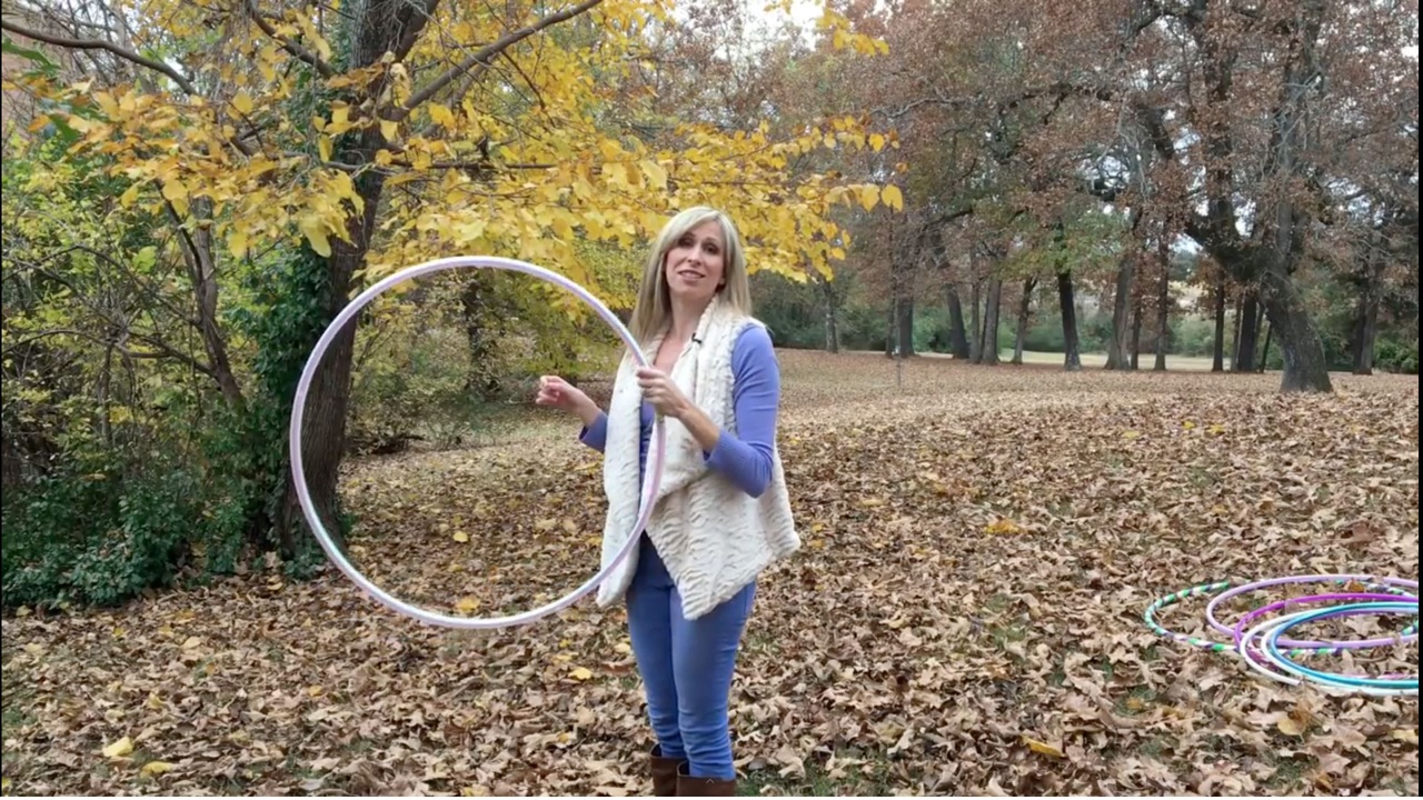 Michele McCoy demonstrating a behind-the-back hoop juggle toss outdoors.