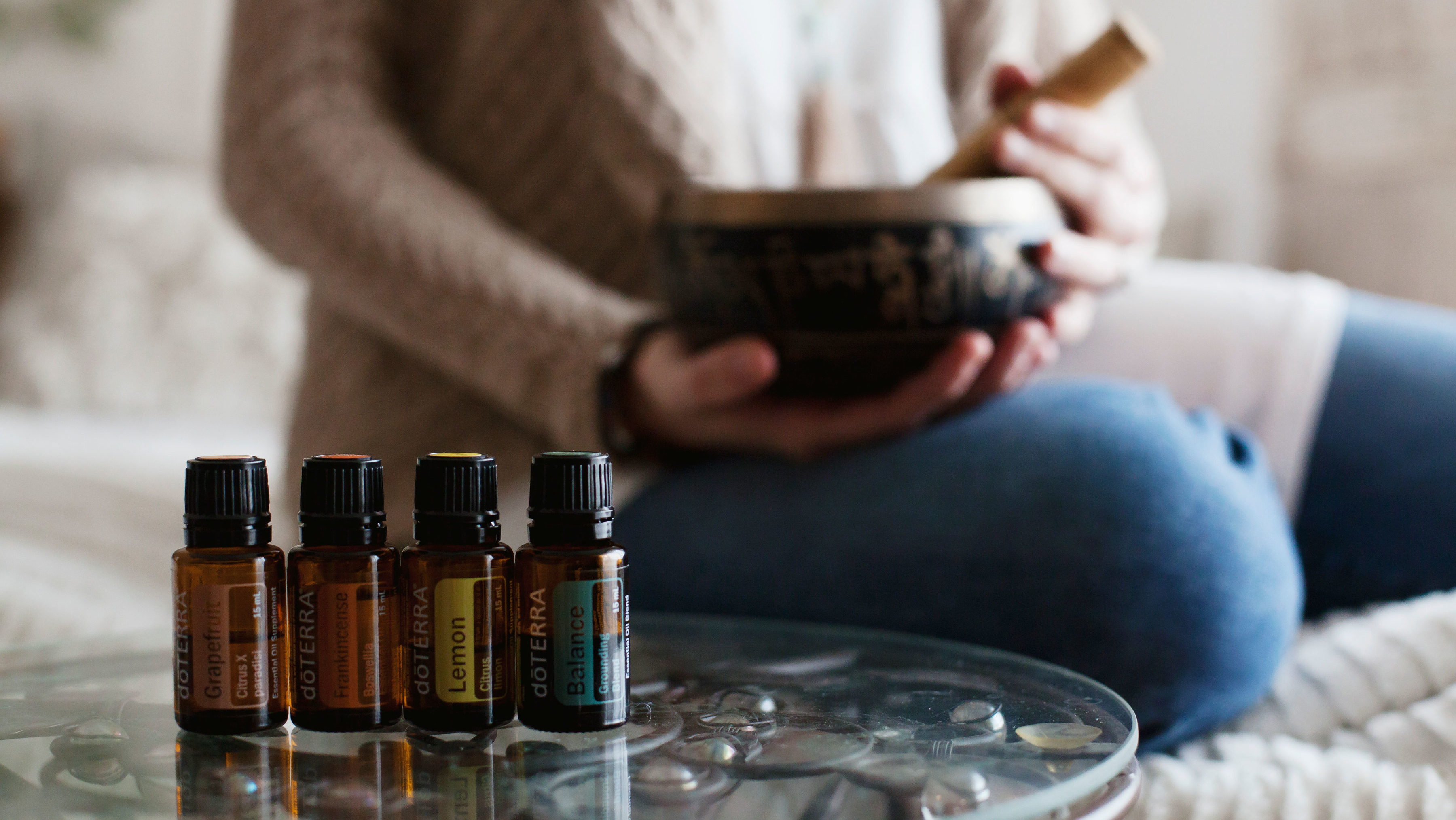 Essential oil bottles on a table beside a person holding a bowl