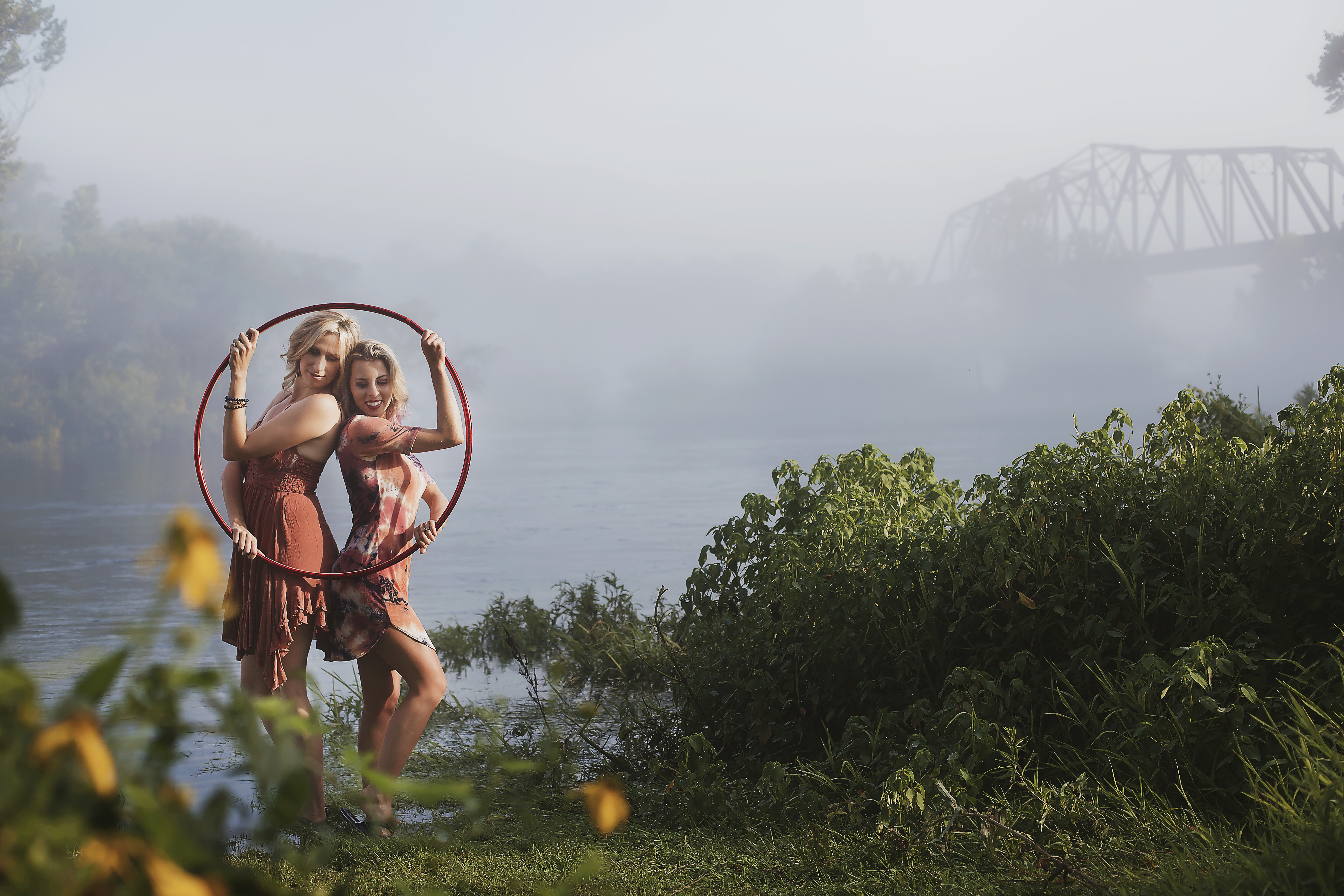 Katie Sunshine and Michele McCoy posing together inside a red hoop by the river